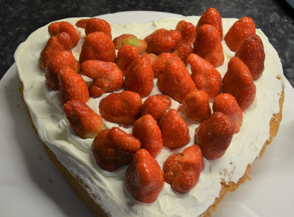 Mother's Day Cake, a heart shaped cake topped with whipped cream and strawberries, presented on a flat plateau.