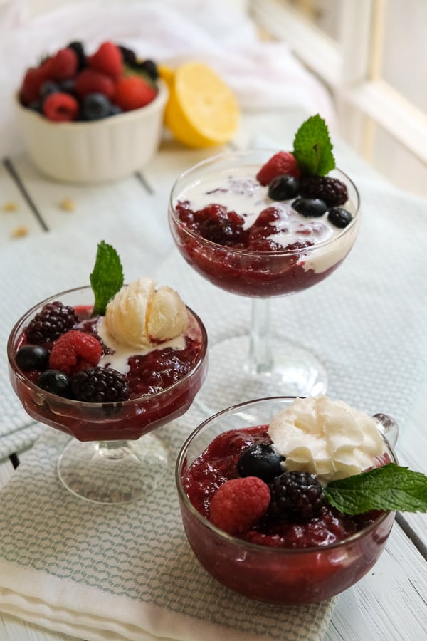 Rote Grutze by International Desserts Blog, 3 glas desserts bowls with rote grutze topped with fruit and vanilla ice cream and a leaf of mint