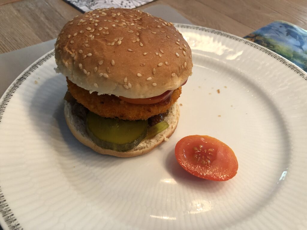 Vegetarian Chilli burger, served on a white plate with a slice of tomato next to it.