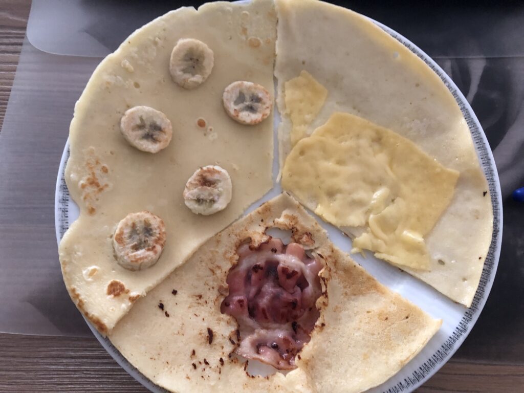 Pancakes, served on a white plate. 1/3 with cheese, 1/3 with bacon and 1/3 with banana