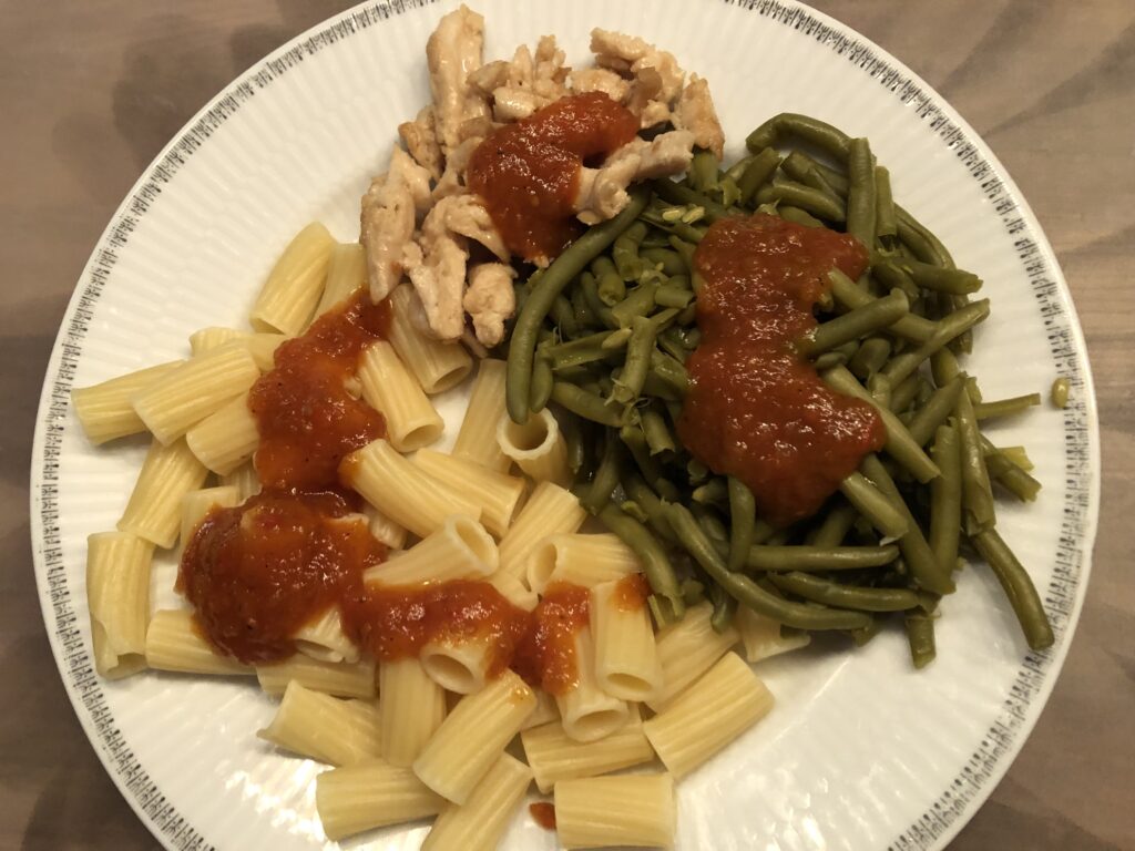 Pasta, vegetarian chicken and green beans with barbecue sauce, served on a white plate
