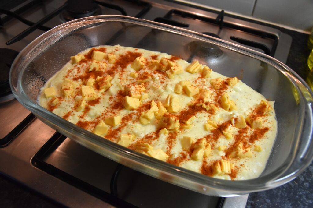 Topped with cheese and paprika, in a casserole dish standing on the stove
