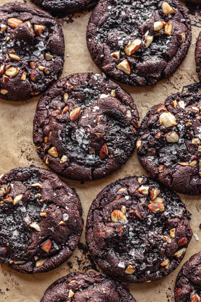 Dark Chocolate Almond Cookies by The Cozy Plum, One cookie in the middle completely visible, 5 partly visible around that cookie