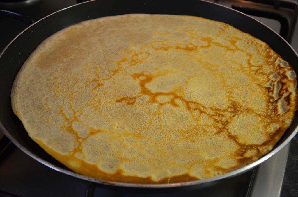 The pancake is flipped, still in a pancake frying pan